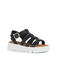 Sandali neri in pelle con più cinturini e una fibbia laterale. Presentano una suola piatta bianca con scanalature texturizzate e una soletta color marrone.