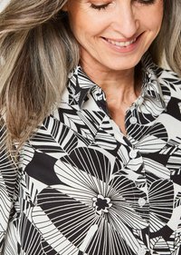 Camicia a righe bianco e nero con motivi floreali e geometrici, dotata di colletto e chiusura con bottoni, realizzata in tessuto liscio.