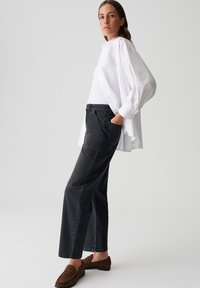 Jeans neri a gamba larga abbinati a una camicia bianca morbida, con dettagli come bottoni e una sfumatura texturizzata, indossati con mocassini marroni.