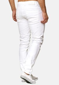 Jean en denim blanc avec une coupe slim, des poches arrière et un patch logo sur la taille. Le design est épuré, avec une texture lisse et sans motifs visibles.