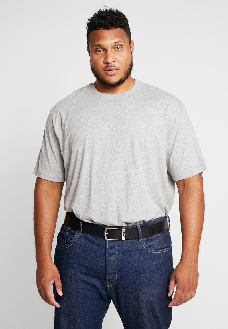T-shirt gris à manches courtes avec un col rond, porté avec un jean en denim bleu et une ceinture noire avec une boucle en argent.