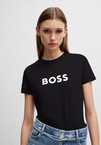 T-shirt noir à manches courtes avec "BOSS" imprimé en lettres blanches en gras sur la poitrine, associé à un short en denim bleu clair.
