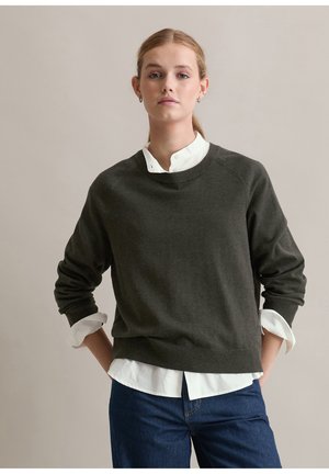 Pull vert foncé en texture douce avec des manches longues et un col rond, superposé sur une chemise blanche à col ; coupe décontractée.
