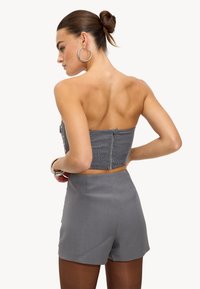 Haut court froncé gris avec fermeture éclair au dos, assorti à un short gris taille haute. Texture lisse, design minimaliste, et boucles d'oreilles argentées en forme d'anneau.