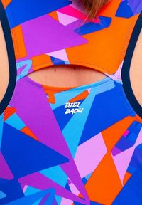 Kleurvolle sporttanktop met een blauw, paars, oranje en roze geometrisch patroon en een open rug; het logo leest "BIDI BADU."