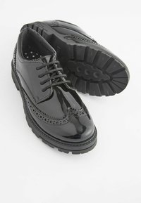Chaussures noires en cuir verni avec des détails de brogue, dotées d'une semelle en caoutchouc robuste et de lacets. L'intérieur est en tissu à motif étoilé.