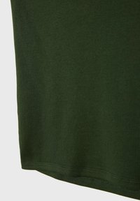 Tessuto a coste verde scuro, primo piano di un orlo di t-shirt con una finitura liscia e dettagli di cucitura visibili. Design semplice e aderente.