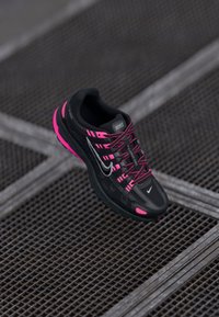 Fekete Nike sportcipő rózsaszín díszítéssel, texturált hálós felsőrész, fényvisszaverő logó és párnázott talp. Az cipőfűző kontrasztos színű.