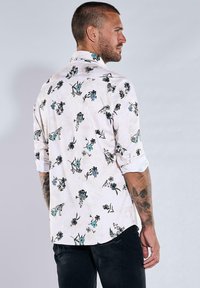 Langärmliges Hemd aus leichtem Stoff mit floralem Muster, das blaue und schwarze Blumen zeigt, mit Knopfkragen und hochgerollten Ärmeln.