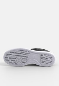 Podeszwa buta z wzorzystym bieżnikiem w białej gumie, z czarną górną częścią z logo "New Balance" i akcentami. Gładka tekstura.