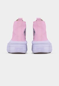 Ζευγάρι ροζ Converse μποτάκια ψηλού τύπου, που βλέπουν από πίσω, δείχνοντας χοντρές λευκές σόλες και θηλιές για τράβηγμα στις φτέρνες.