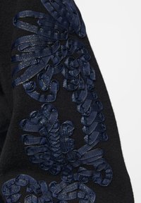 Tissu noir ornée d'une broderie en ruban bleu marine complexe au design floral, mettant en valeur des boucles texturées et des accents détaillés tout au long.