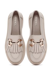 Chaussures en cuir beige à enfiler avec un design à franges et un accent en métal rose doré. Semelle en caoutchouc texturé, forme arrondie et finition lisse.