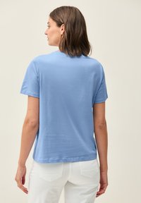 Camiseta de manga corta azul claro hecha de algodón suave. Presenta un corte relajado con dobladillo recto y un clásico cuello redondo.