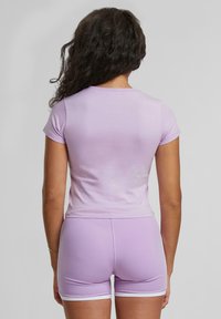 T-shirt fitted color lilla con maniche corte, texture liscia. Abbinato a pantaloni corti lilla con bordi bianchi e una vestibilità aderente.