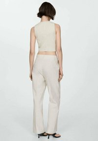 Top corto a rayas color crema con tirantes anchos, combinado con pantalones de talle alto y corte relajado. El material parece ligero y transpirable.