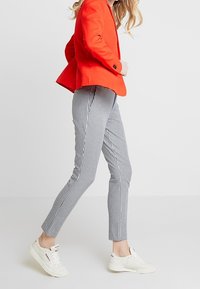 Punainen bleiseri, mustavalkoruudulliset housut, valkoiset tennarit. Bleiseri on räätälöity yksirivisellä napilla; housut ovat kapeat ja lyhyet.