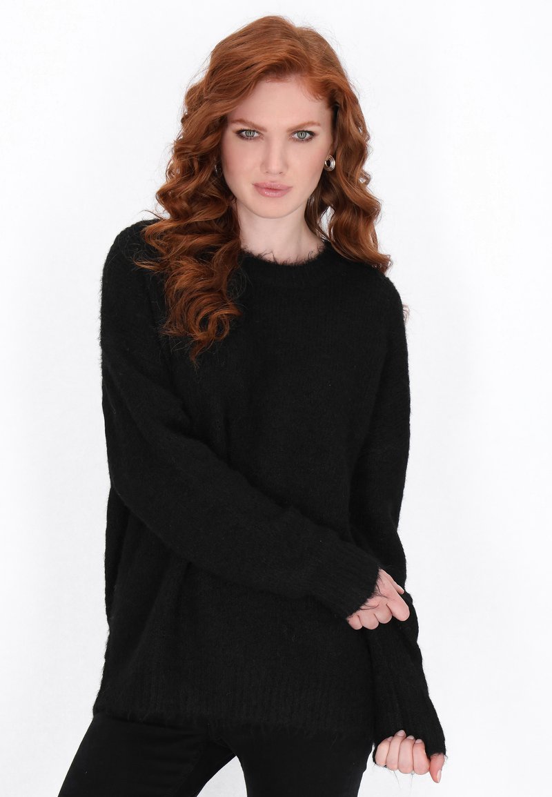 Maglione nero, sovradimensionato, a maglia con maniche lunghe, orlo a coste e una consistenza morbida e pelosa. Indossato con pantaloni neri.