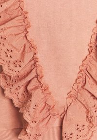 Maglione rosa con colletto arricciato, caratterizzato da motivi floreali ricamati, realizzato in un tessuto morbido con una consistenza liscia e orlo a costine.