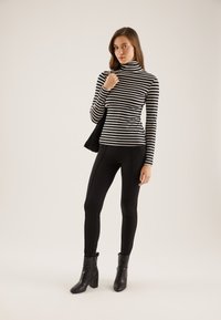 Svart og hvit stripete turtleneck, tettsittende stil, kombinert med svarte leggings og høye svarte støvler, båret med en svart veske.