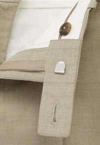 Beżowa tkanina o gładkiej fakturze, z białą podszewką, brązowym guzikiem i srebrnym akcentem. Wzór zawiera przeszyty pasek.