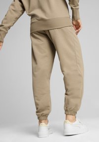 Beige-housut, joissa on elastiset hihnat ja vyötärö, valmistettu pehmeästä kankaasta. Yhdistetty valkoisiin lenkkareihin, joissa on paksu pohja ja vaaleat yksityiskohdat.