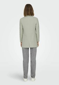 Svetlo zelena krojena jakna s slim fit krojem, dolgimi rokavi in z odprtino na hrbtu, v kombinaciji s sivimi teksturiranimi hlačami in belimi supergami.