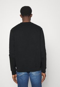 Sudadera negra de manga larga, con cuello redondo, textura suave. Diseño minimalista, sin logotipos ni patrones visibles. Llevada con jeans azules.