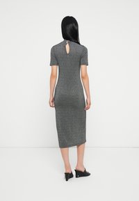 Šedé žebrované midi šaty s krátkým rukávem; mají výřez na zádech s knoflíkem a přiléhavý siluetu. Nosené s černými klínovými botami.