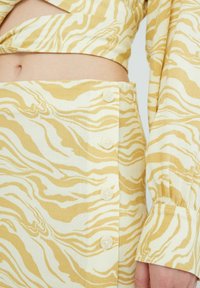 Twee-delige outfit met een geel en witte zebra print. De crop top heeft lange mouwen, terwijl de rok knopen aan de zijkant heeft.