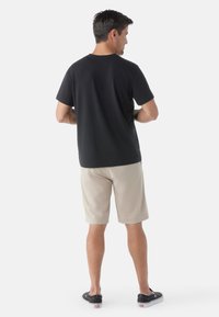 Black cotton T-shirt, short sleeves, relaxed fit, paired with beige shorts. Black sneakers with white soles add contrast to the outfit.