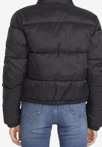 Veste matelassée noire avec un design court, dotée d'une texture matelassée, d'un ourlet élastique et d'un col montant. Couture visible accentue les détails.