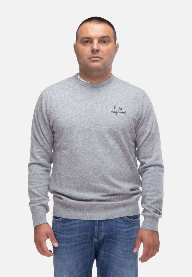 Maglione grigio a maglia con collo rotondo, caratterizzato da testo ricamato sul lato sinistro del petto e polsini e orlo a coste. Indossato con jeans blu.
