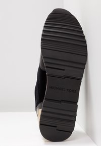 Semelle d’une chaussure noire Michael Kors avec motif antidérapant texturé et nom de la marque embossé au centre de la semelle en caoutchouc.