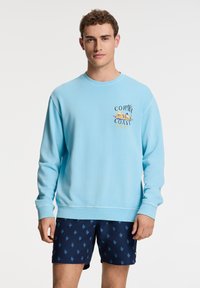 Felpa azzurra con polsini e orlo a coste, dotata di un design stampato. Abbinata a pantaloni corti blu navy con un sottile motivo corallo.