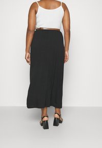 Zwarte maxi-rok met een vloeiende uitstraling, gemaakt van zachte stof, met een elastische tailleband en gedragen met zwarte hakken.