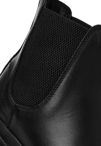 Bottines noires à cheville avec tige en cuir lisse et panneau élastique texturé pour un enfilage facile. Design élégant avec un bout arrondi.