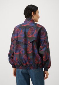 Colorful, lightweight jacket with a floral pattern in red and purple on a dark background. Features an elastic waistband and a relaxed fit.
