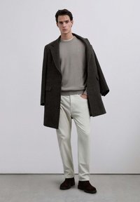 Ciemnoszary wełniany płaszcz na jasnoszarym swetrze, w połączeniu z białymi spodniami i brązowymi zamszowymi butami. Płaszcz ma duże guziki i kieszenie.