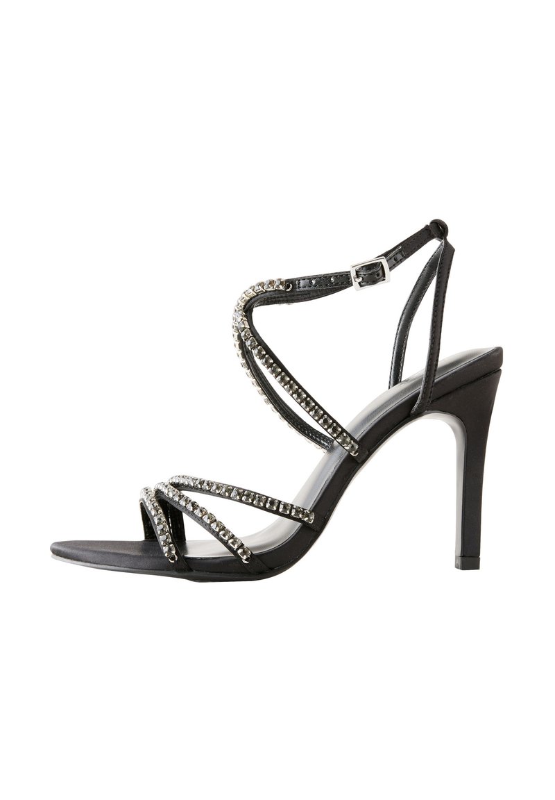 Črna sandaleta s peto z več prekrižanimi trakovi, okrašena z metalnimi poudarki in kristalčki. Eleganten dizajn z zašiljenim prstom in tanko peto.