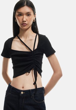 Sort ribbet crop top med korte ærmer, med firkantet udskæring, snøre detaljer i siden og justerbare stropper. Parret med denim jeans.