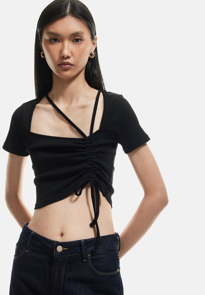 Sort ribbet crop top med korte ærmer, med firkantet udskæring, snøre detaljer i siden og justerbare stropper. Parret med denim jeans.
