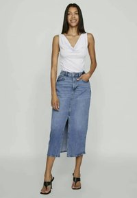 Λευκό τοπ με λαιμόκοψη τύπου κάβουρα, μπλε τζιν μίντι φούστα με μπροστινή σχισμή, συνδυασμένο με μαύρες σανδάλια με λουριά. Απλός σχεδιασμός, ανεπίσημο στυλ.