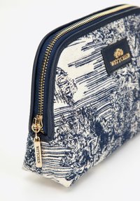 Borsa cosmetica navy e crema con un motivo testurizzato, cerniera dorata e un'etichetta con logo del marchio. Progettata in una forma curvata per un facile accesso.