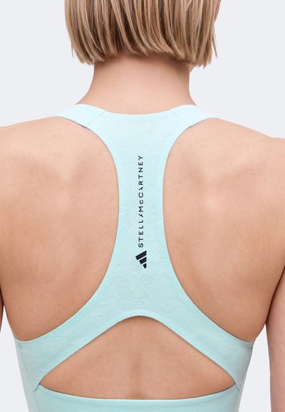 Rückenansicht einer Person, die ein hellblaues Stella McCartney Racerback-Sporttop mit strukturiertem Stoff und Logo-Schriftzug in der Mitte trägt.
