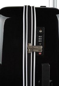 Maleta rígida negra con rayas blancas, doble zipper y cerradura de combinación. Presenta un acabado texturizado y acentos de hardware resistente.