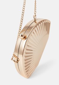 Kultainen metallinen clutch-laukku, jossa on uurrettu auringonsädekuvio, pyöreä muoto ja ketjusankaa. Varustettu pyöreällä soljella.