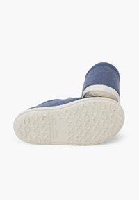 Botte en toile bleue avec un bout rond et une semelle en caoutchouc blanche, présentant un motif texturé sur la partie inférieure et une petite étiquette indiquant la taille 24.