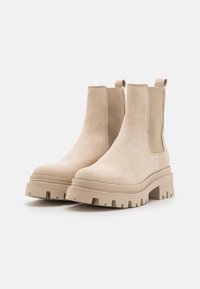 Beige Wildleder Stiefeletten mit elastischen seitlichen Einsätzen, strukturiertem Gummisohlen und einem klobigen Plattform-Design, ausgestattet mit Zuglaschen an der Rückseite.
