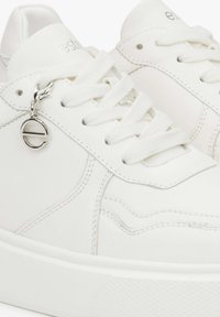 Białe skórzane sneakersy z teksturowanymi detalami, okrągłym noskiem, płaskimi białymi sznurówkami i srebrnym zawieszką z logo po boku. Gładkie wykończenie powierzchni.